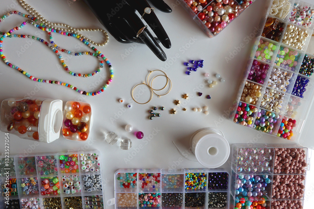 Hand figurine, colorful friendship bracelets, necklaces, various beads and DIY supplies on the table. Making jewelry at home. Flat lay.