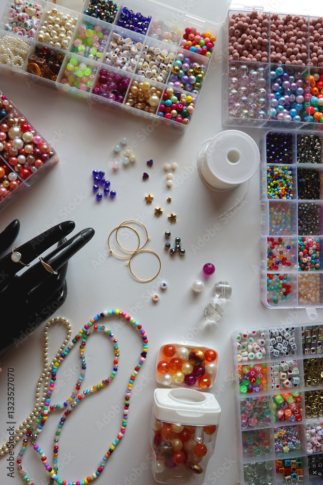 Hand figurine, colorful friendship bracelets, necklaces, various beads and DIY supplies on the table. Making jewelry at home. Flat lay.