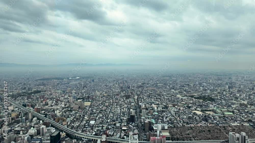 Elevated highway curving through a dense cityscape in Osaka, Japan, with mountains visible in the distance under a cloudy sky Elevated highway curving through a dense cityscape in Osaka, Japan, with mountains visible in the distance under a cloudy sky