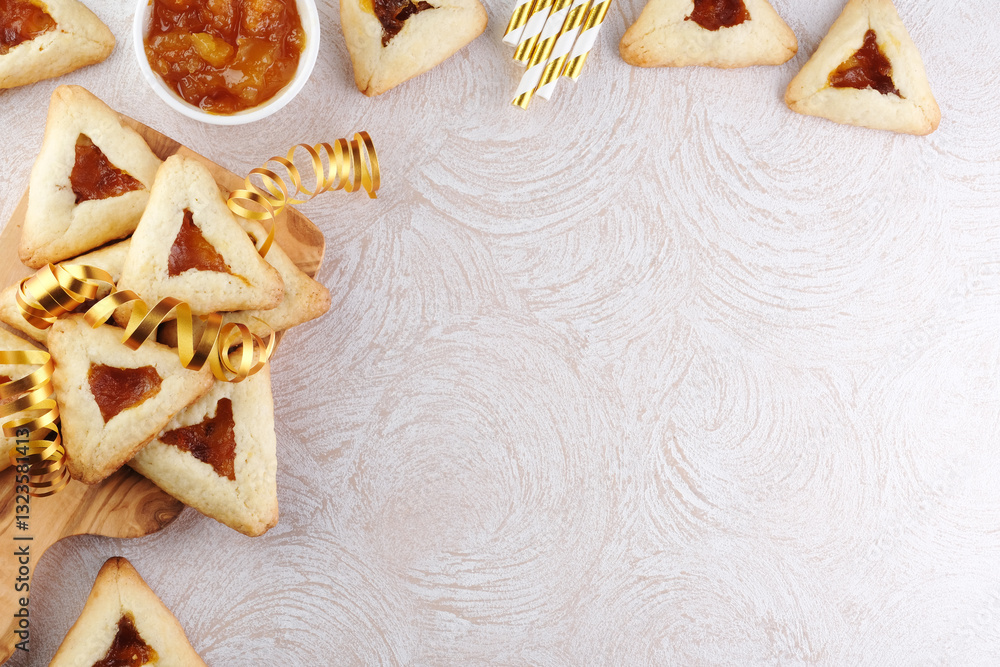 Fototapeta premium Close up freshly baked triangular cookies filled with fruit surrounded by golden decorations ribbon on a wooden cutting board. Purim celebration concept. top view. space for text