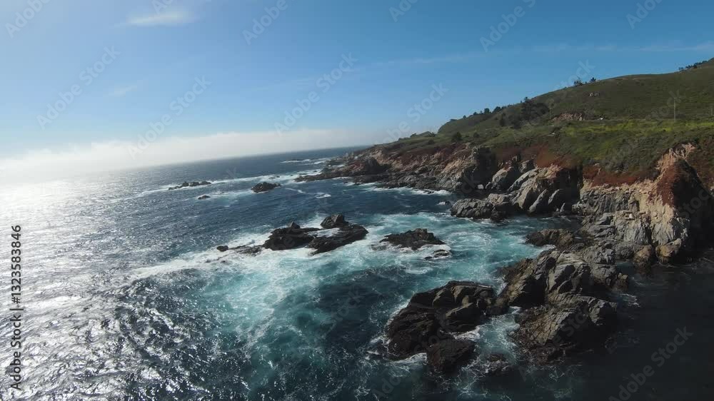 A scenic view of the California coastline where waves crash against rugged rocky cliffs. The deep blue ocean stretches to the horizon under a clear sky. A scenic view of the California coastline where waves crash against rugged rocky cliffs. The deep blue ocean stretches to the horizon under a clear sky.