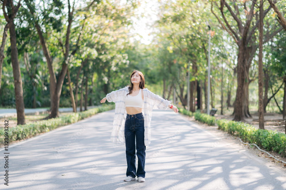 Asian woman enjoying summer while breathing fresh air in serene park, surrounded by lush green trees and sunlight filtering through Asian woman enjoying summer while breathing fresh air in serene park, surrounded by lush green trees and sunlight filtering through