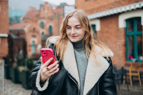 Obraz na płótnie Laughing young woman taking selfie on the urban background. Cute beautiful woman using mobile phone. 30s girl recording self video, talking on online call w salonie