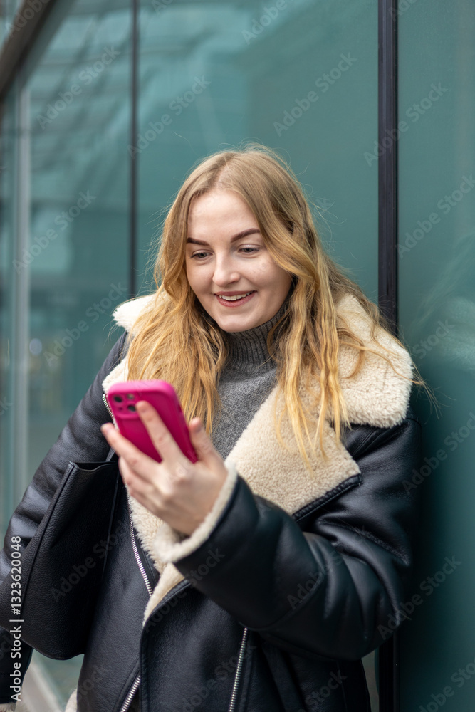 Young stylish 30s woman writes message on smartphone walking on city street. Urban lifestyle concept. Autumn time. Charming female wearing stylish outfit chatting online. High quality photo.