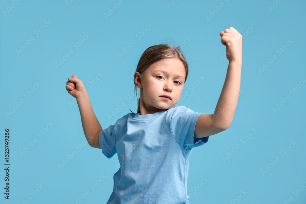 Cute little girl showing her biceps on light blue background Cute little girl showing her biceps on light blue background