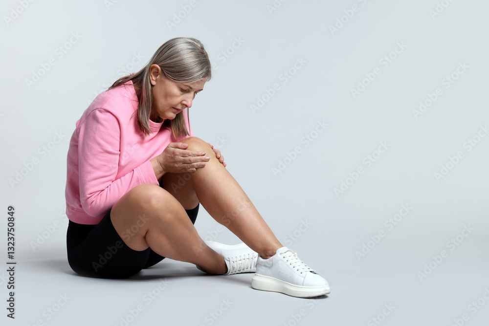 Senior woman suffering from knee pain on light grey background. Space for text Senior woman suffering from knee pain on light grey background. Space for text