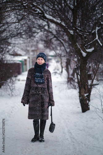 Obraz na płótnie A woman in a karakul fur coat walks along a snow-covered path, surrounded by deep snowdrifts that blanket everything in sight. w salonie