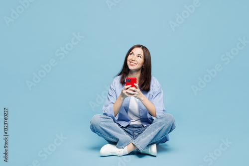 Fotografie Full body young woman she wears shirt casual clothes sit hold in hand use mobile cell phone look aside on area isolated on plain pastel light blue cyan background studio portrait