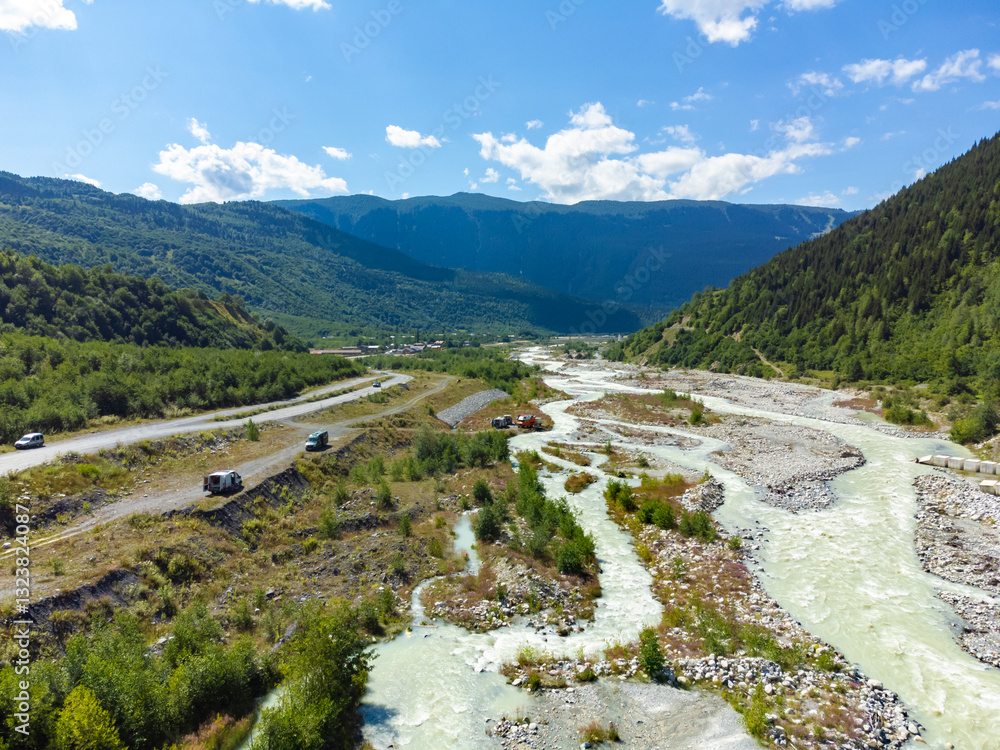 Breathtaking aerial view of a pristine river winding through a lush green valley, surrounded by towering peaks of the caucasus mountains, creating a picturesque landscape under a vibrant blue sky