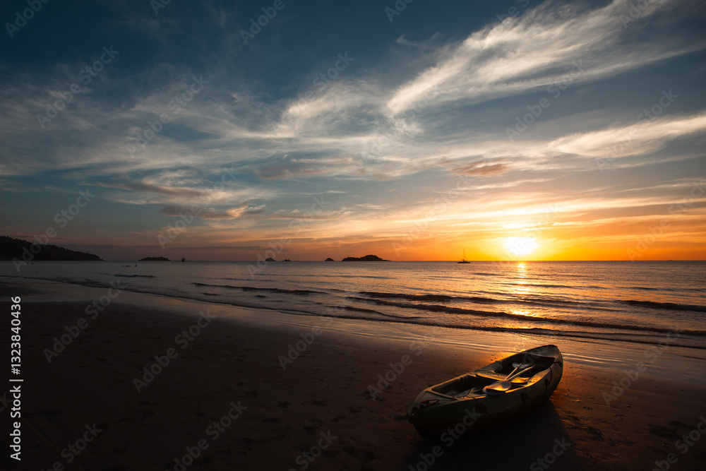 A kayak rests on the sandy shore of the sea during an amazing sunset, with vibrant colors painting the sky.