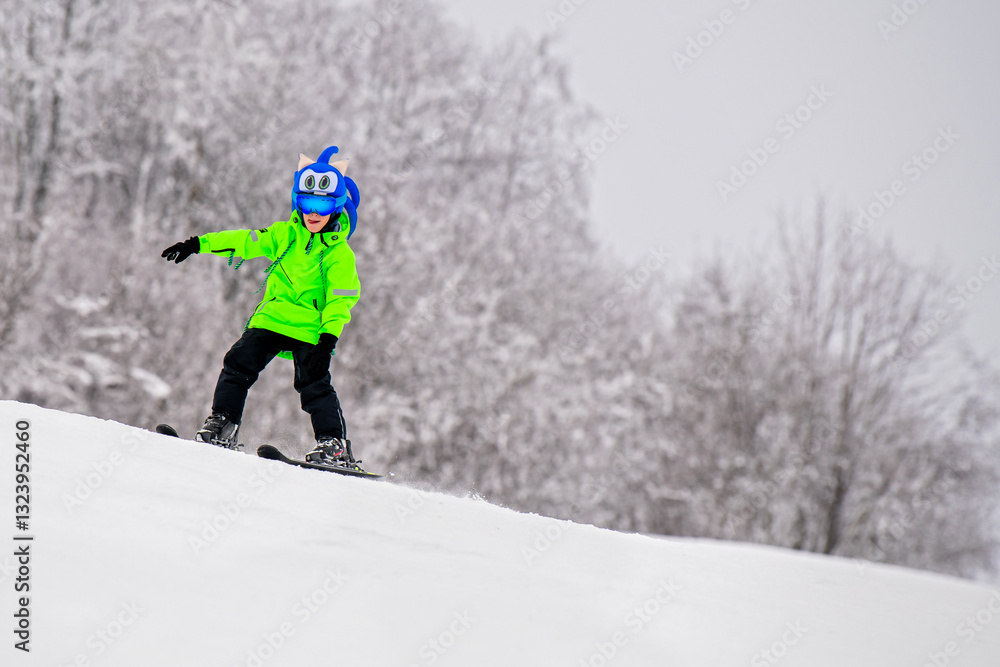Young skier in a bright neon jacket and fun character helmet skiing down a snowy slope. Exciting winter sports Young skier in a bright neon jacket and fun character helmet skiing down a snowy slope. Exciting winter sports
