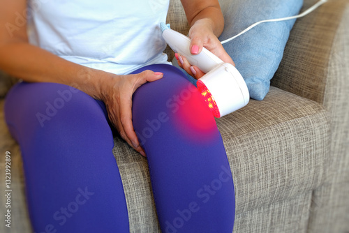 A woman uses an innovative red light therapy device on her knee to effectively relieve pain and relieve inflammation of the injured knee