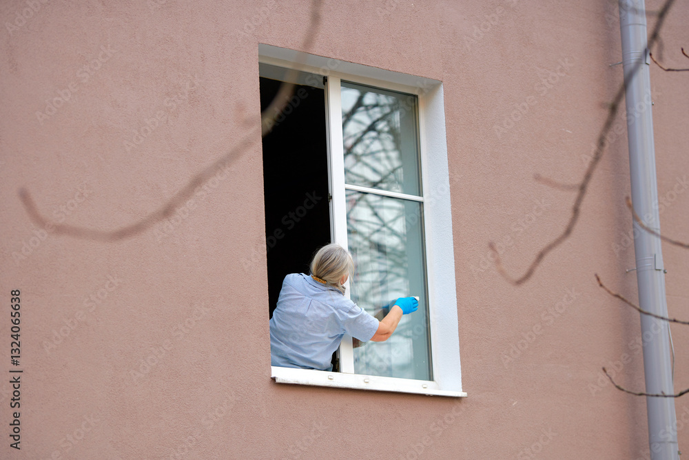 Senior female wiping glass window while leaning forward, home cleaning risks, fall prevention, potential dangers of falling. Woman washing window at height, home maintenance risks. Accident prevention