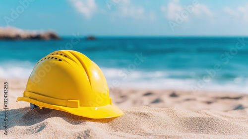 A yellow hard hat rests on sandy beach, contrasting with the vibrant blue ocean and clear sky, symbolizing construction and leisure.