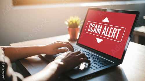 Person using laptop displaying a scam alert warning on screen, signifying online security, internet fraud prevention, and digital safety awareness