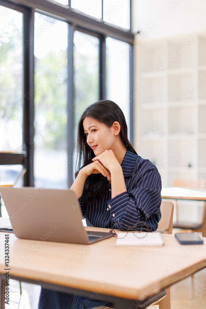Portrait of Business Asian woman sitting at at laptop and thinking of problem solution, working schedule for employee writing report into notebook while using laptop computer in coworking space Portrait of Business Asian woman sitting at at laptop and thinking of problem solution, working schedule for employee writing report into notebook while using laptop computer in coworking space