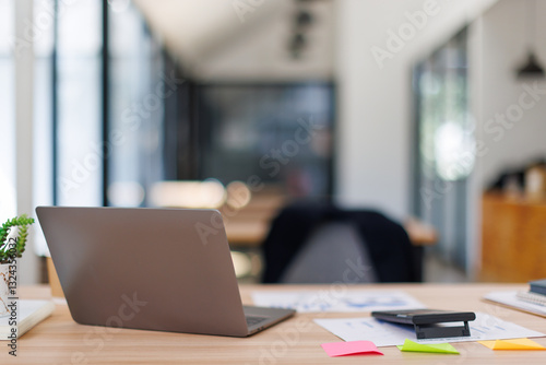 Laptop Computer, notebook, and eyeglasses sitting on a desk in a large open plan office space after working hours	