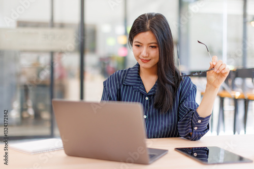 Asian businesswoman sits at desk with laptop online using internet and notepad happily recording receipt contact information online delivery.
