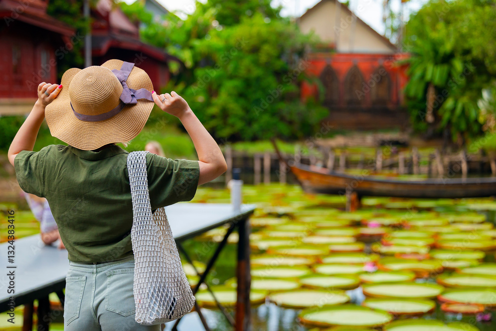 Fototapeta premium Back view Woman in hat exploring exotic water lily pond in phuket, thailand. Travel in nature of thai photo