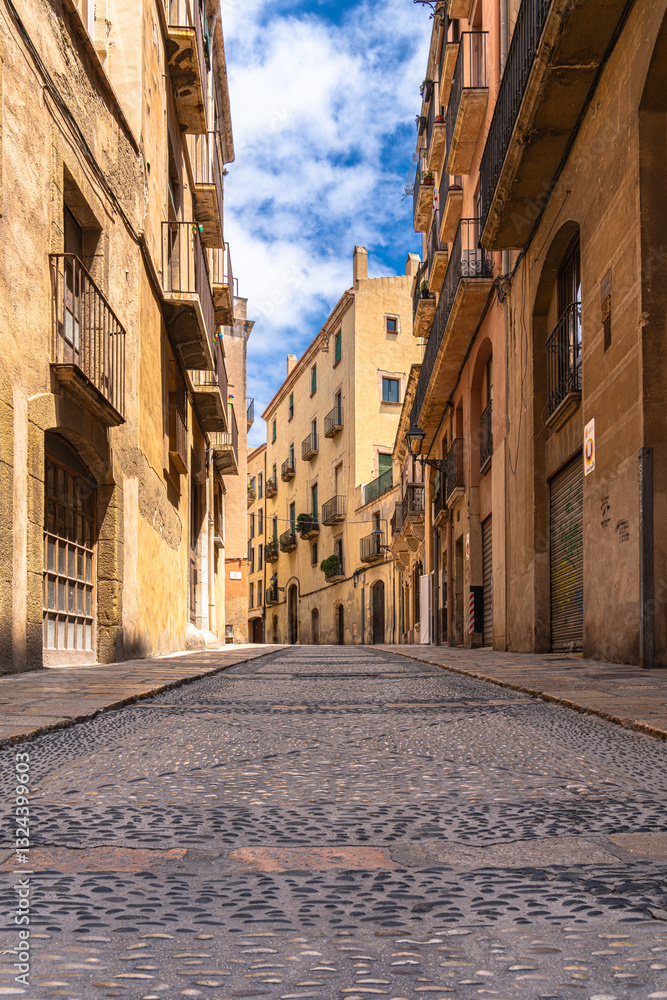 Obraz premium Low angle view of small alley in pedestrian area in old town of Tarragona city, on a sunny day in summer, Tarragona, Catalonia, Spain