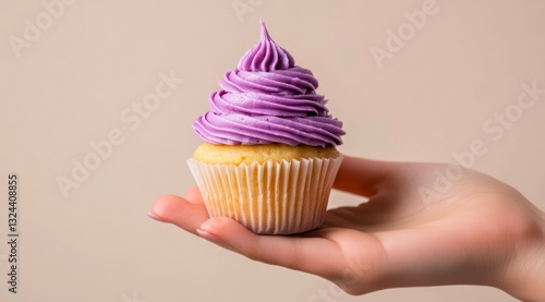 Female hand holding vanilla cupcake with purple cream frosting.