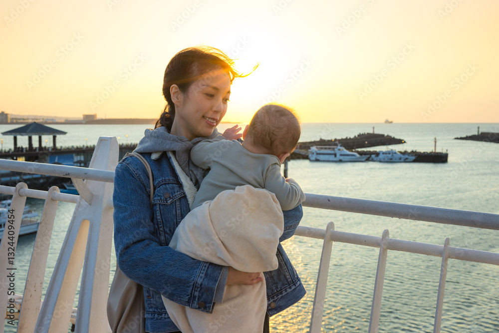 Woman carrying baby enjoying ocean sunset view