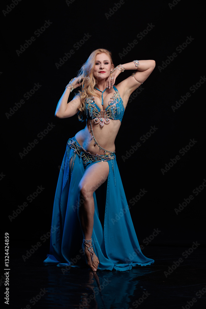 Obraz premium Woman in a blue costume oriental dancer posing and dancing on a black background