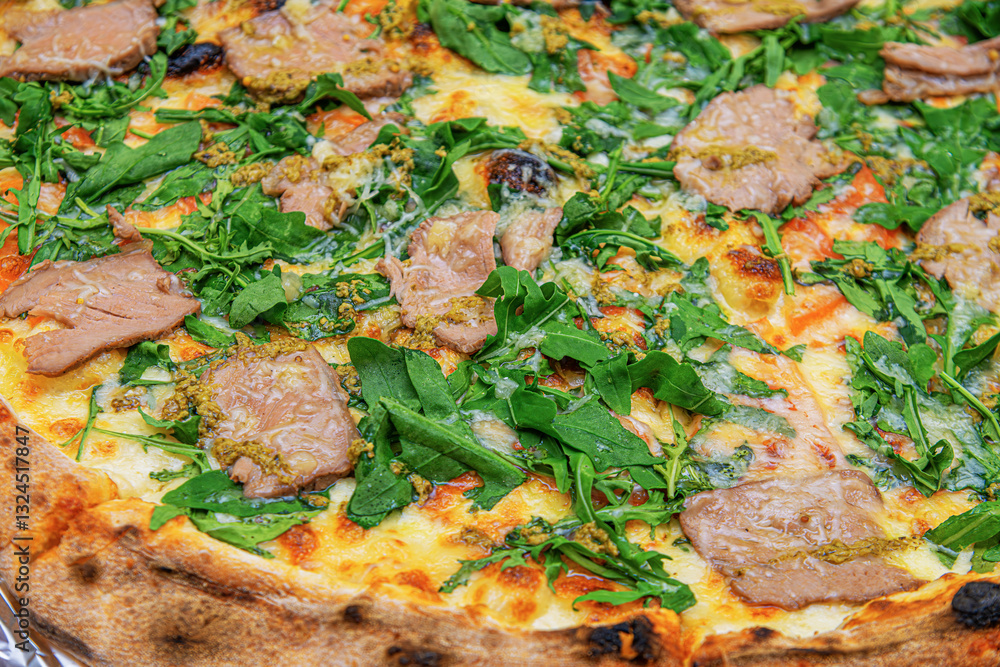 A close-up of a gourmet pizza topped with fresh arugula, tender slices of meat, and melted cheese on a crispy, golden crust.