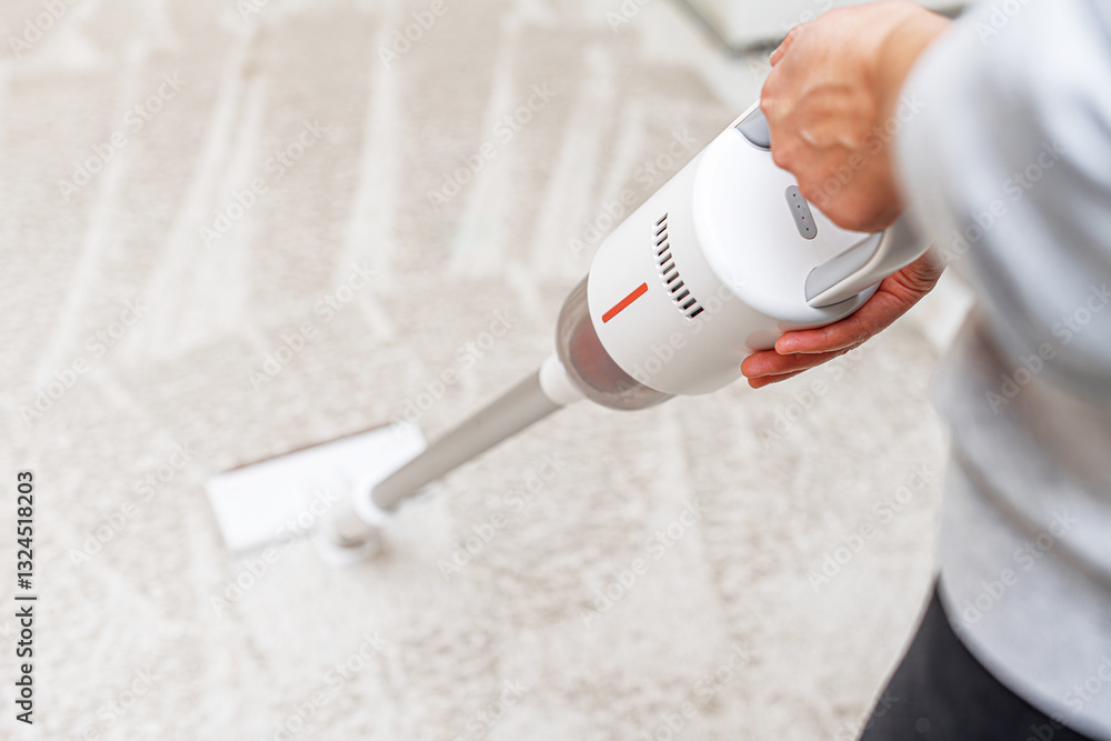 A person is using a modern, cordless vacuum cleaner to clean a carpet, ensuring a dust-free and hygienic home environment.