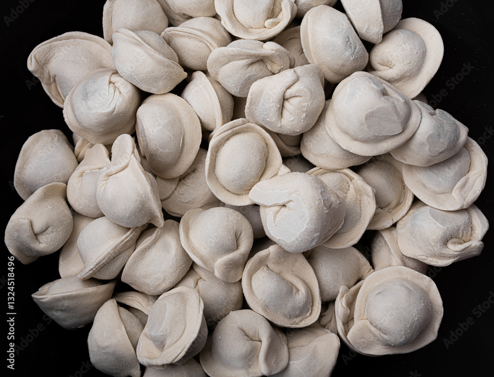 A close-up of a pile of frozen pelmeni, traditional dumplings made from dough and meat filling, resting against a dark background.
