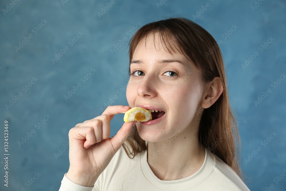 Beautiful woman eating tasty mochi on blurred blue background Beautiful woman eating tasty mochi on blurred blue background