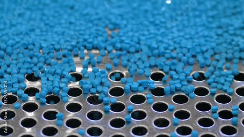 Plastic recycling machine: blue propylene or polyethylene pellets, recycled plastic granules on vibrating shale shaker, conveyor belt: close up. Separation, sustainable and waste reduction concept