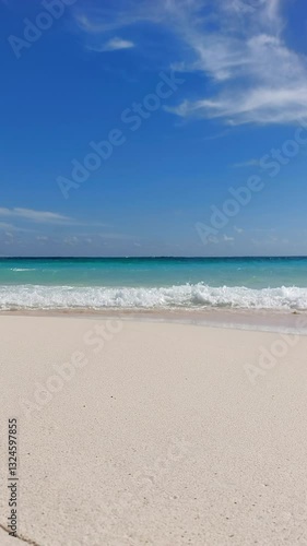 HD vertical video on a sandy tropical deserted beach with gentle waves crashing on the shore. In the background the turquoise Caribbean Sea and blue sky. Eco-friendly travel and vacation concept