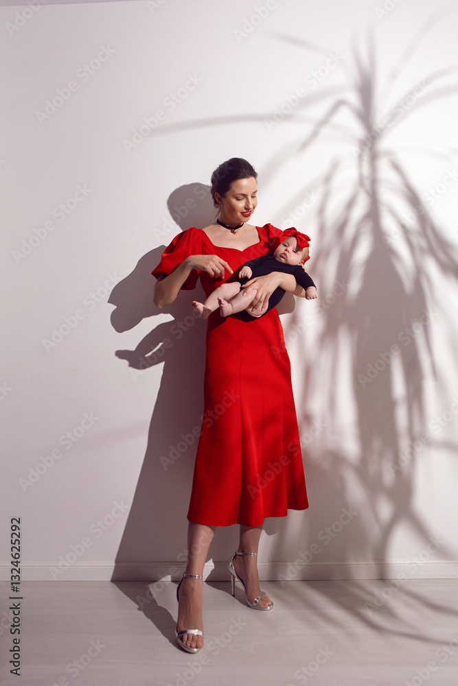 portrait a woman in a red dress holds a child at home on a white background with a shadow from a bush