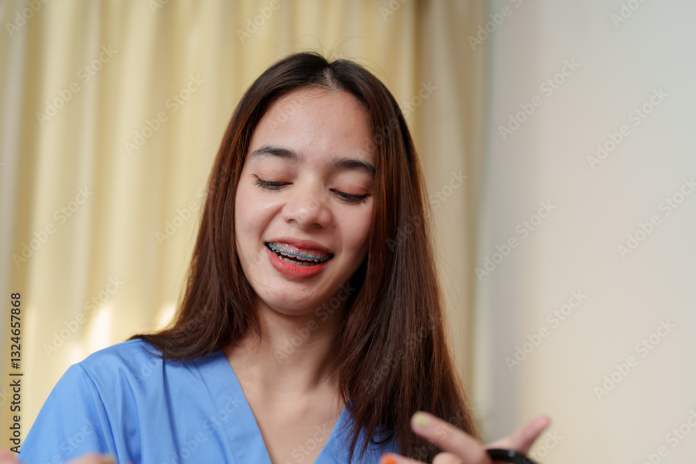 Asian young woman wearing a blue medical scrub, smiling with eyes closed while enjoying a relaxing moment. Long brown hair, natural beauty, and braces, feeling refreshed during a holiday. Asian young woman wearing a blue medical scrub, smiling with eyes closed while enjoying a relaxing moment. Long brown hair, natural beauty, and braces, feeling refreshed during a holiday.
