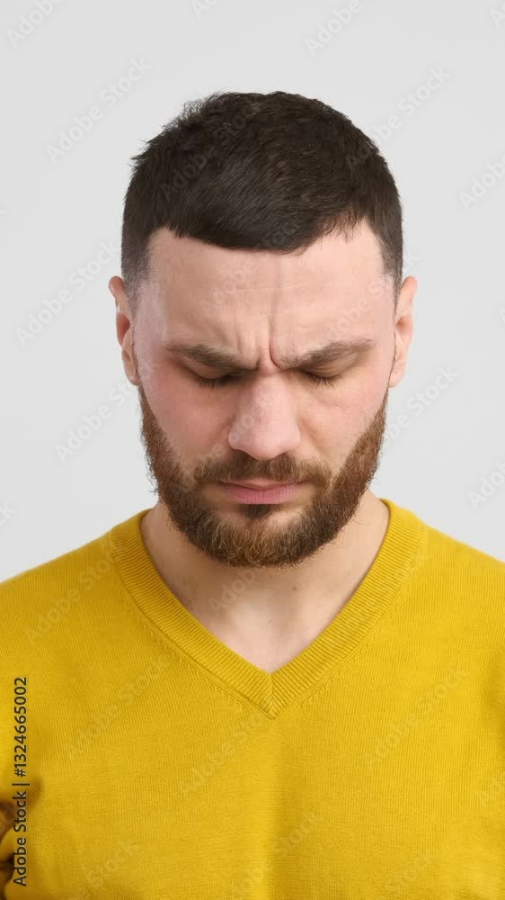 Tired and unwell caucasian man felling sick and suffering from a migraine on a white background. Annoyance and stress affecting well-being. Vertical video. Tired and unwell caucasian man felling sick and suffering from a migraine on a white background. Annoyance and stress affecting well-being. Vertical video.