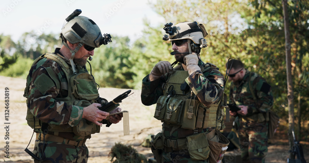 Fototapeta premium Soldiers from a powerful army prepare a battle strategy, entering data into the system, discussing tactics, and organizing equipment while dressed in camouflage uniforms and helmets at the training