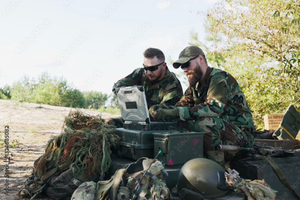 The commander sits at his computer in the field, drafting reports for the army base. A soldier presents a map, and they discuss strategy while troops guard the camp behind them. The commander sits at his computer in the field, drafting reports for the army base. A soldier presents a map, and they discuss strategy while troops guard the camp behind them.