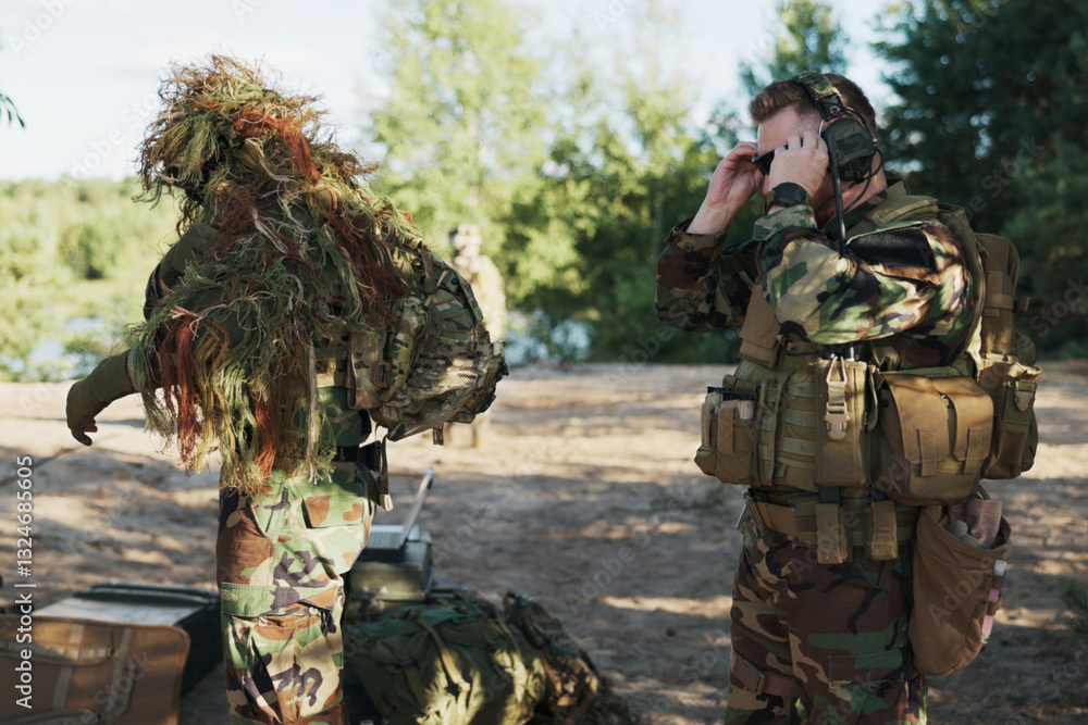 In camouflage uniforms, two soldiers gear up for field exercises, adjusting ammo belts and backpacks, focused on their territorial defense mission near the concealed base. In camouflage uniforms, two soldiers gear up for field exercises, adjusting ammo belts and backpacks, focused on their territorial defense mission near the concealed base.