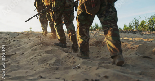Close-up of soldiers footsteps in the sand as they march in formation, military boots pressing into the ground, weapons in hand, patrolling the area during training exercises.