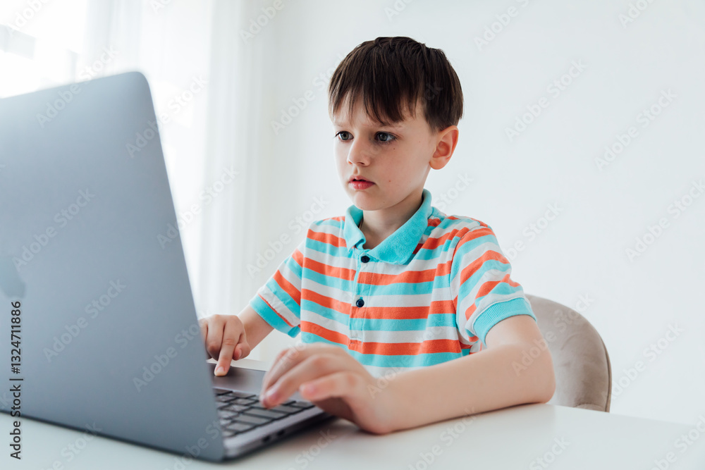 Schoolboy sitting at table with laptop learning games online Schoolboy sitting at table with laptop learning games online