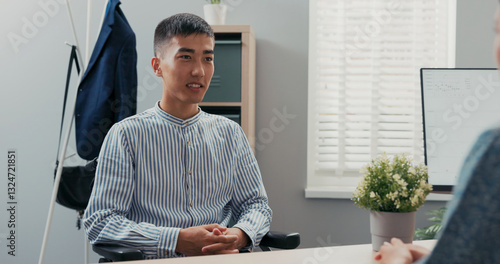 Disabled man dressed in smart blue striped shirt sits at desk in corporate office in wheelchair, he is applying for secretarial job, female corporate executive is conducting interview she ask question