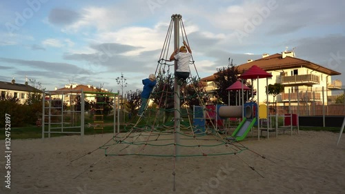 Wallpaper Mural Two kids climbing rope pyramid on modern playground in residential area at sunset. Active children playing outdoors, adventure, and childhood fun. High quality 4k footage Torontodigital.ca