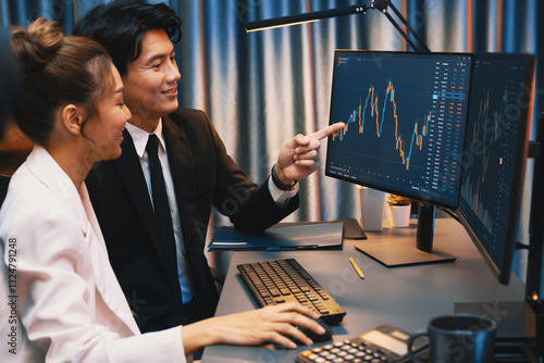 Obraz na plátně Smiling Asian business traders pointing to dynamic stock exchange data screen profit value online website program at night time at home office