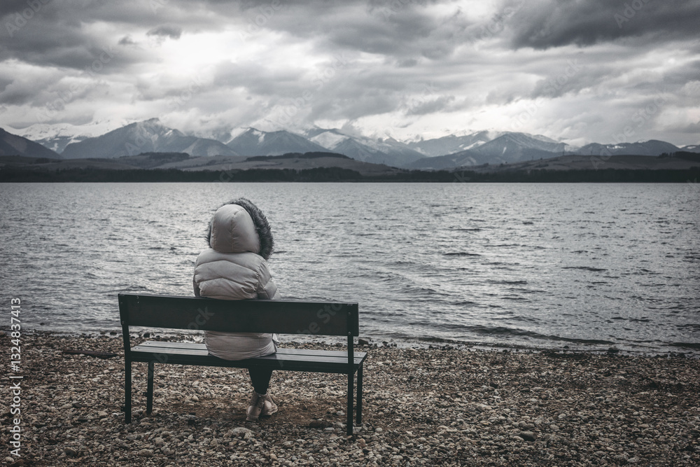 Fototapeta premium Woman in jacket sitting on bench on the shore of the lake
