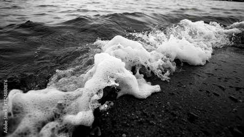 Foamy waves gently embrace a rocky shore, creating a serene dance of water and rock under a moody sky.