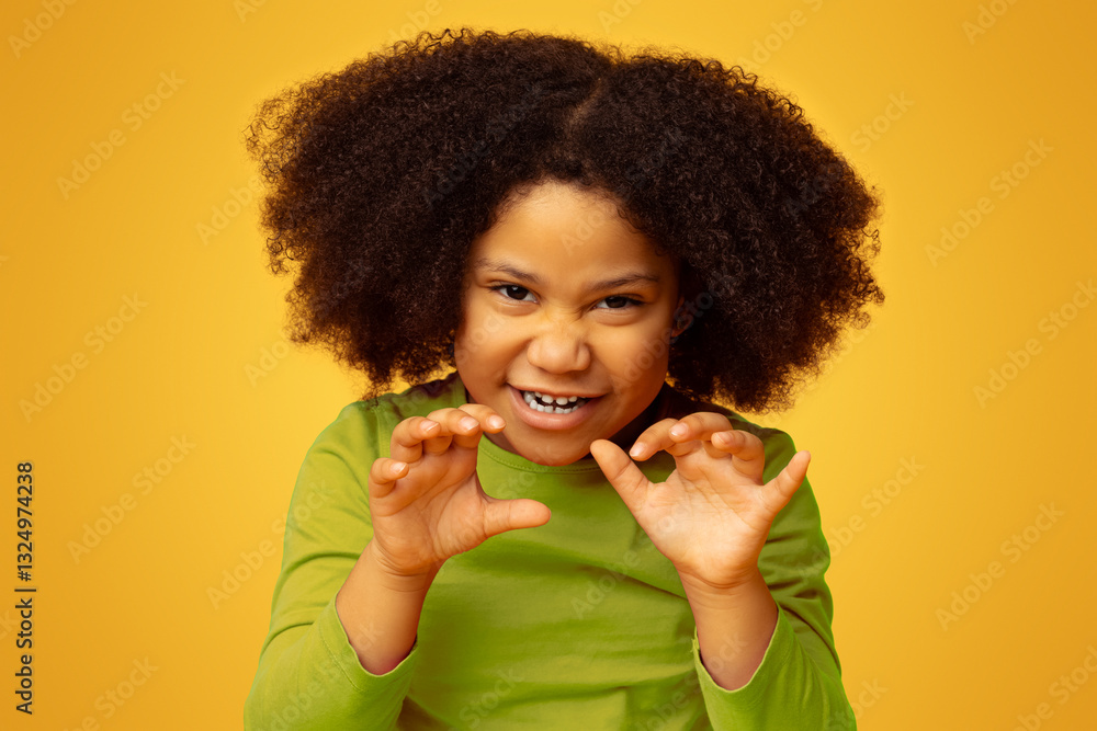 Playful little black girl imitating tiger, roaring and grimacing over yellow studio background Playful little black girl imitating tiger, roaring and grimacing over yellow studio background