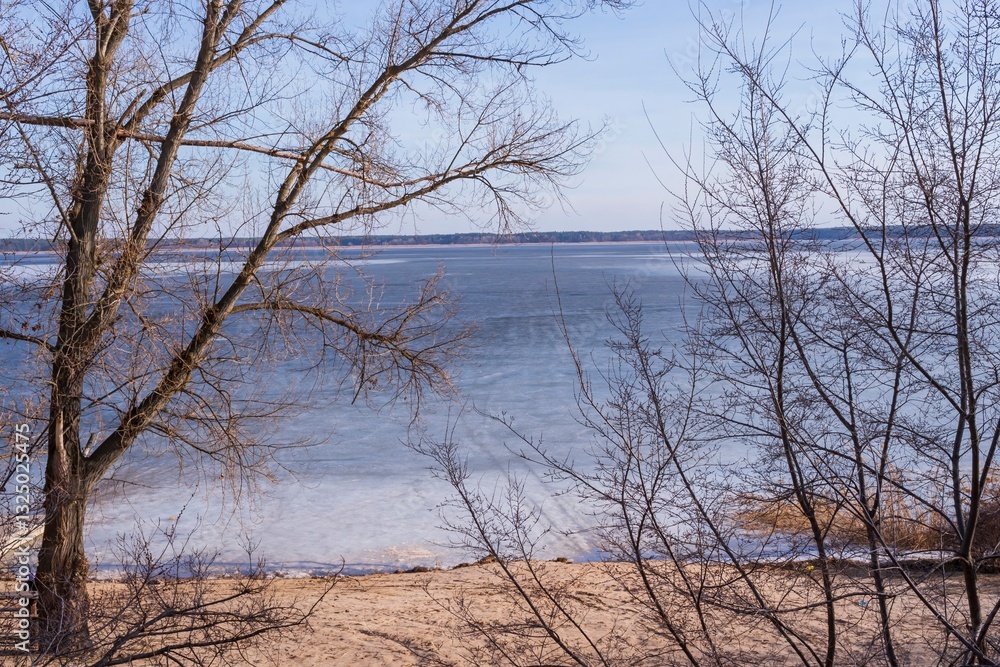 Fototapeta premium Beautiful landscape of a frozen river in early spring. First thawed patches. Sunny spring day