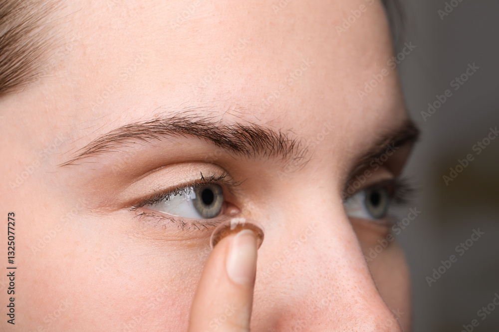 Fototapeta premium Young woman putting in color contact lens on blurred background, closeup