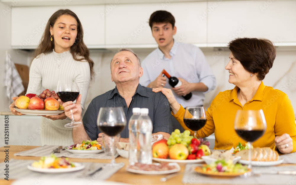 Happy carefree senior parents sharing memories with grown daughter and son-in-law during conversation over family celebration with wine at cozy home environment Happy carefree senior parents sharing memories with grown daughter and son-in-law during conversation over family celebration with wine at cozy home environment